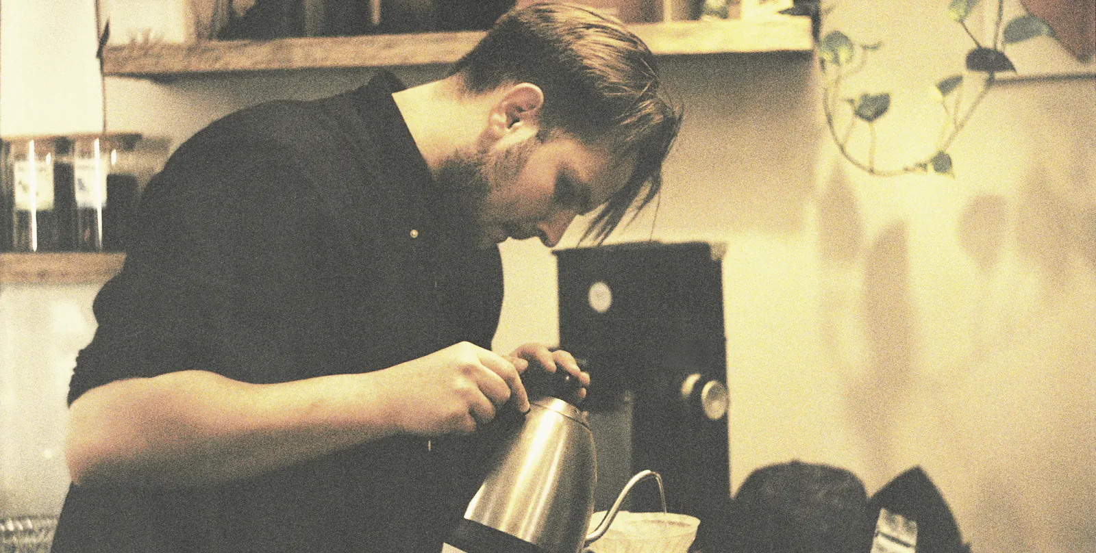 A barista leans over a pour over with a gooseneck kettle