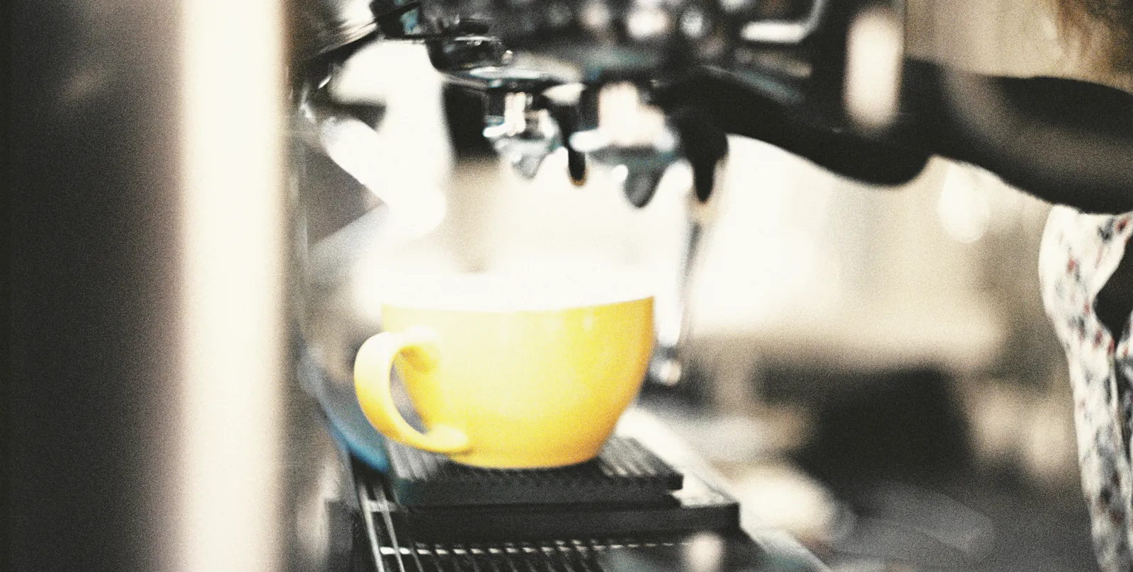A yellow cup waiting under the espresso machine