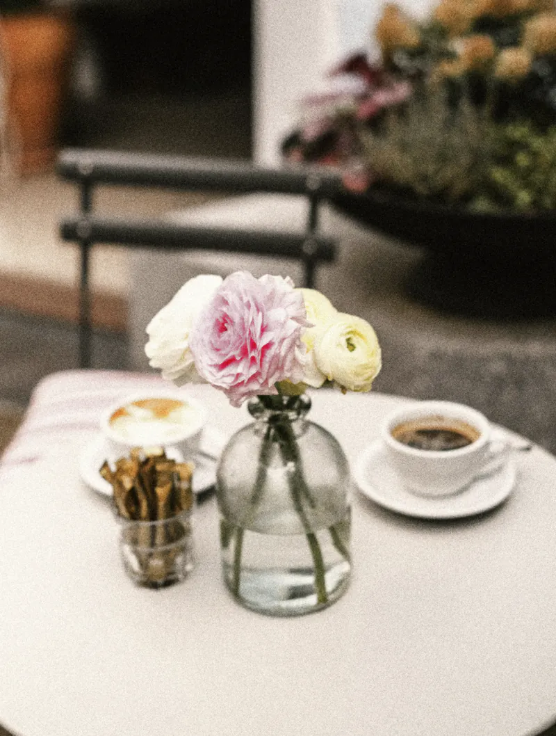 Ranunculus in a glass bottle between two coffees on a small courtyard table