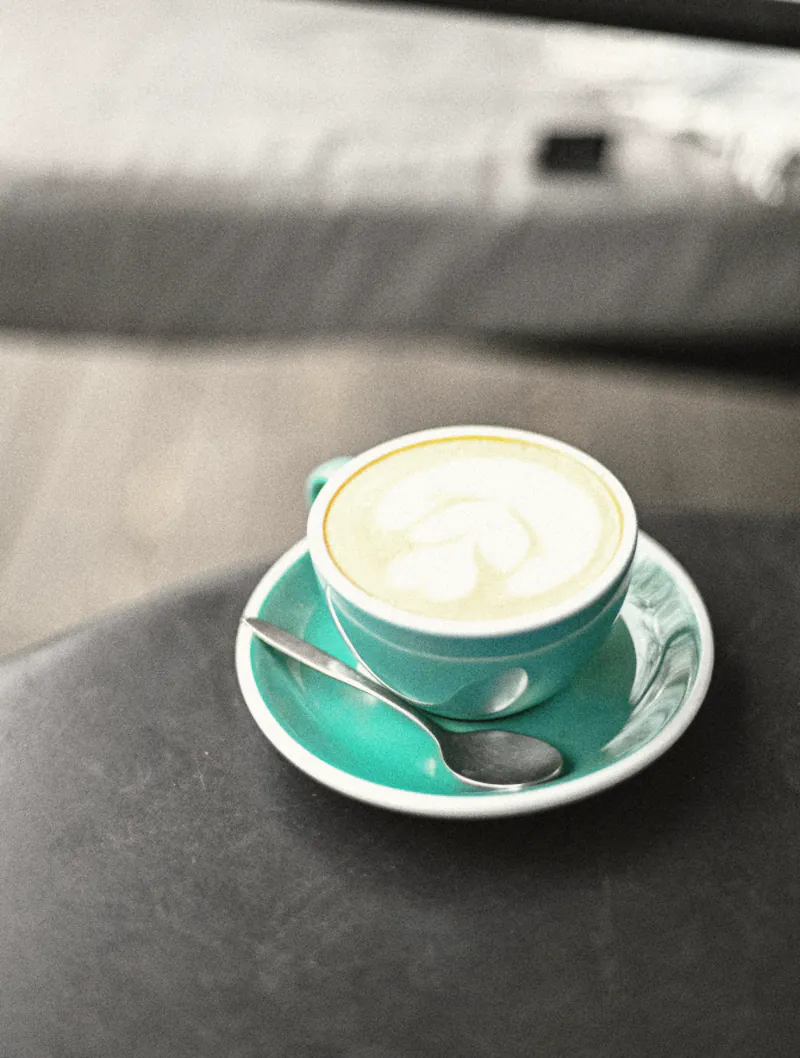 A latte in a teal cup on a dark courtyard table