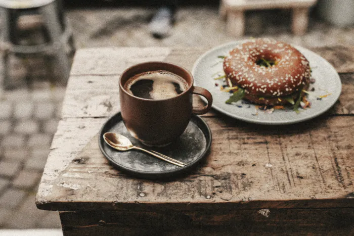 A long black and a sesame bagel on a worn outdoor table