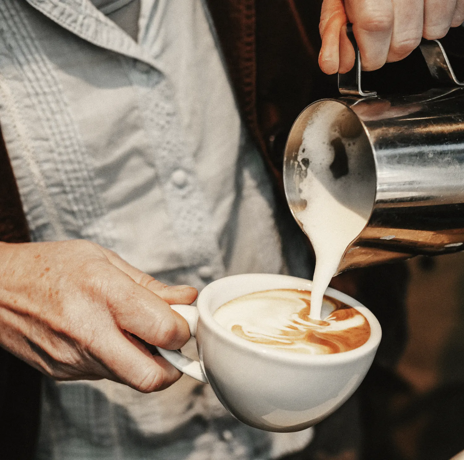 Milk poured from a steel jug into a flat white, close up at the bar