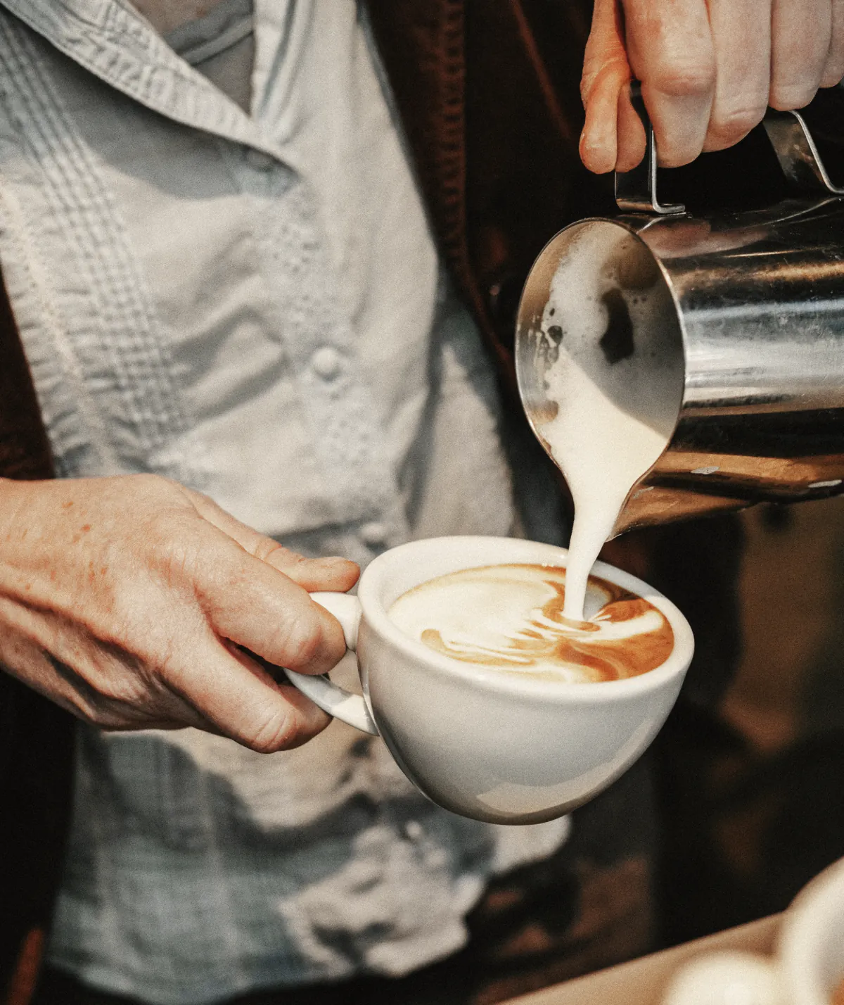 Milk poured from a steel jug into a flat white, close up at the bar