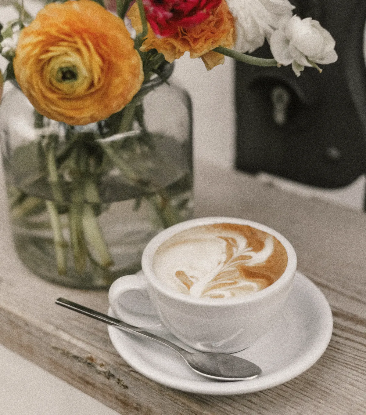 A latte on a timber ledge under a jar of ranunculus