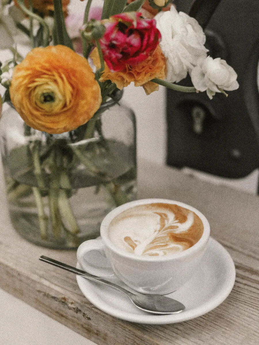 A latte on a timber ledge under a jar of ranunculus