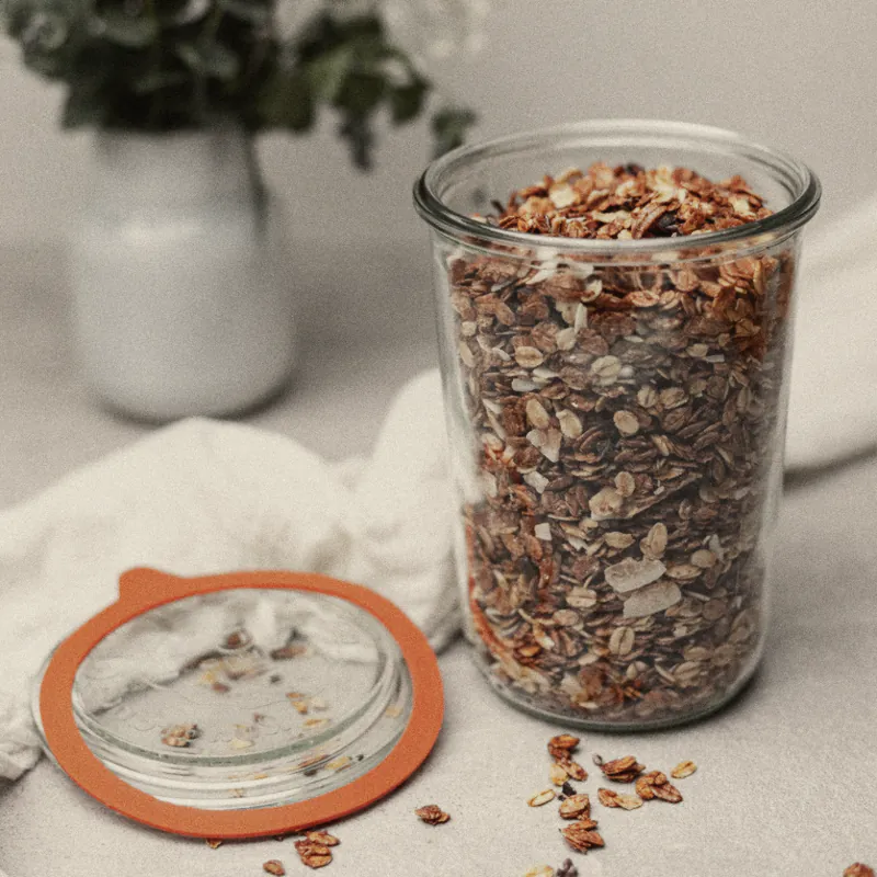House granola in a glass jar, the lid off, beside a jug of roses