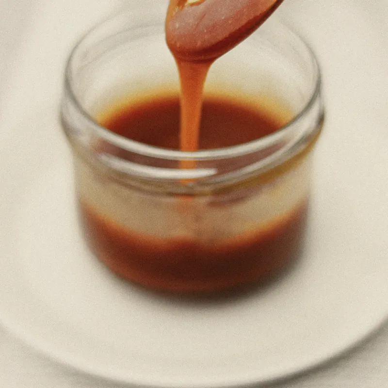 A small jar of honey on a white plate, honey running from a gold spoon into it