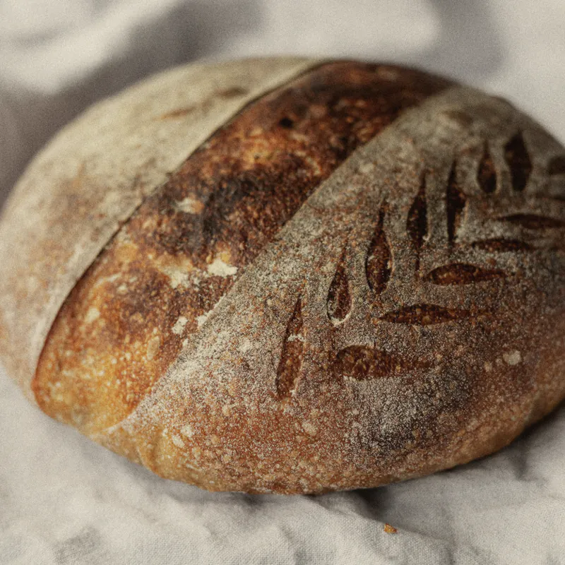 A round sourdough loaf with a scored crust on white linen