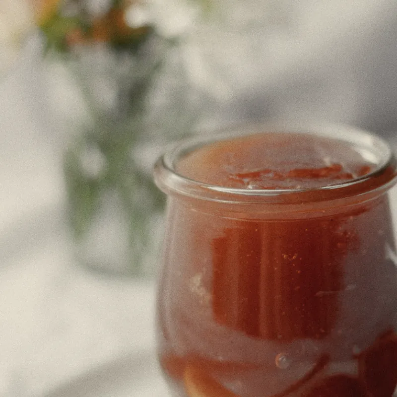 A jar of orange marmalade, a few flowers behind it
