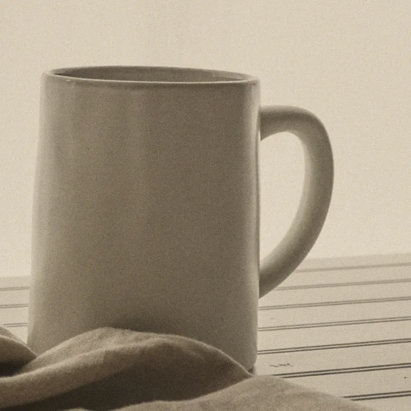 A cream stoneware mug on a linen cloth by the window