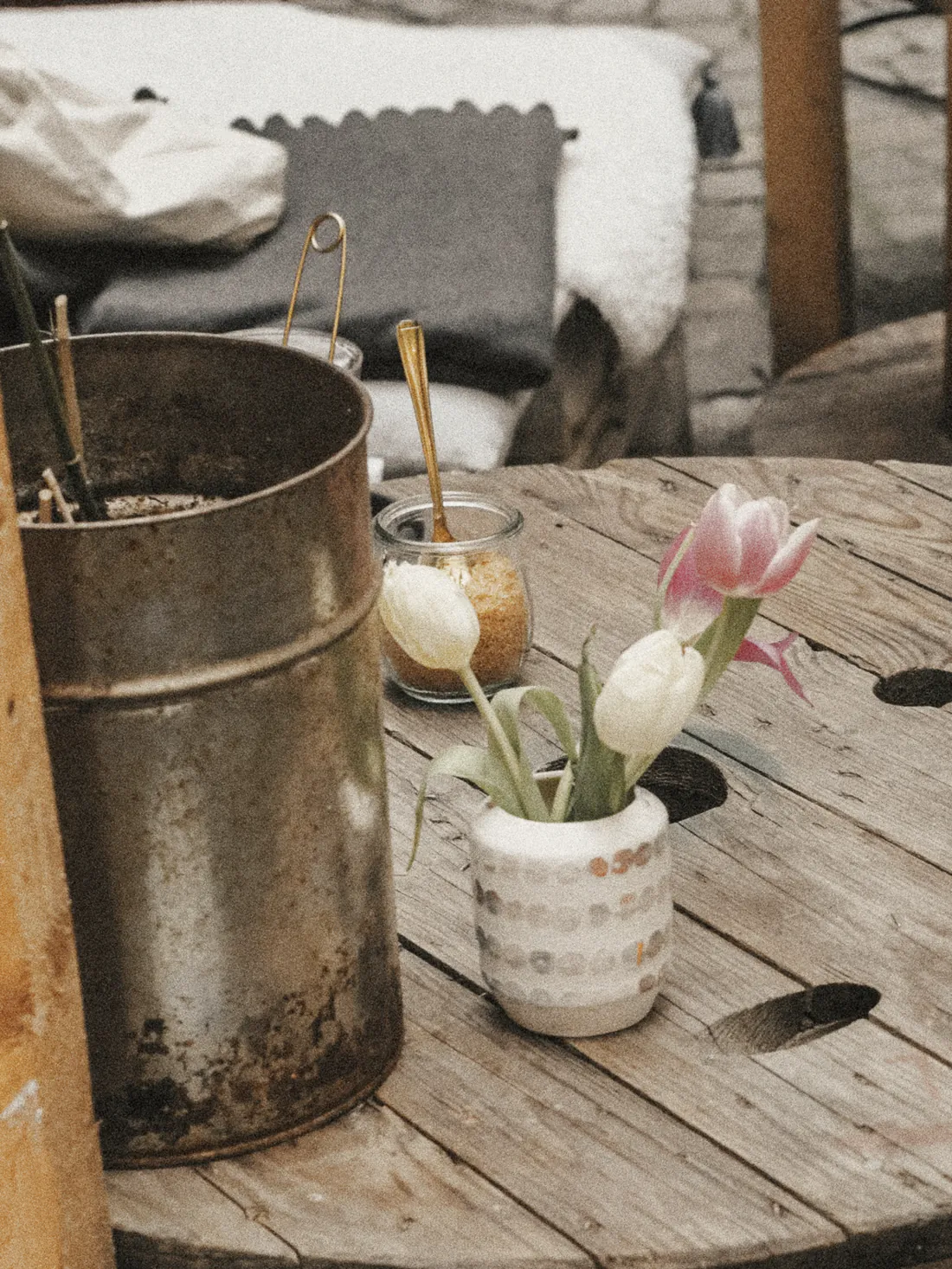 Tulips in a spotted cup on a cable reel table in the lane, a jar of sugar beside them